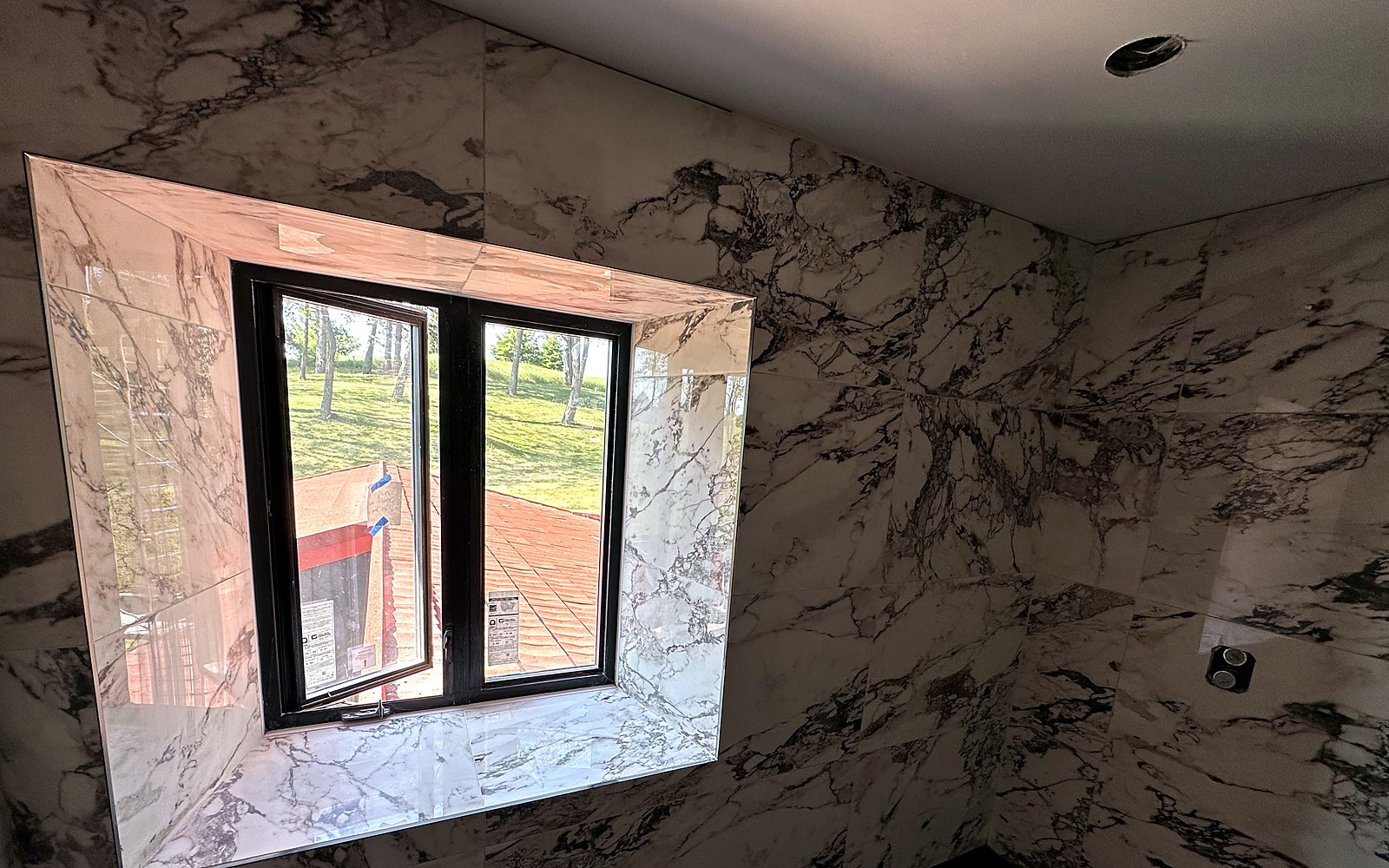 Large-format porcelain wall with book-matched veining carried around a window reveal
